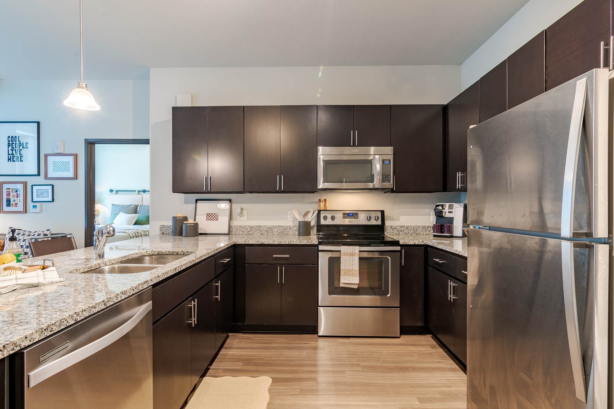 Contemporary kitchen at District Flats Columbia featuring stainless steel appliances, dark wood cabinetry, light countertops, and hardwood-style flooring.