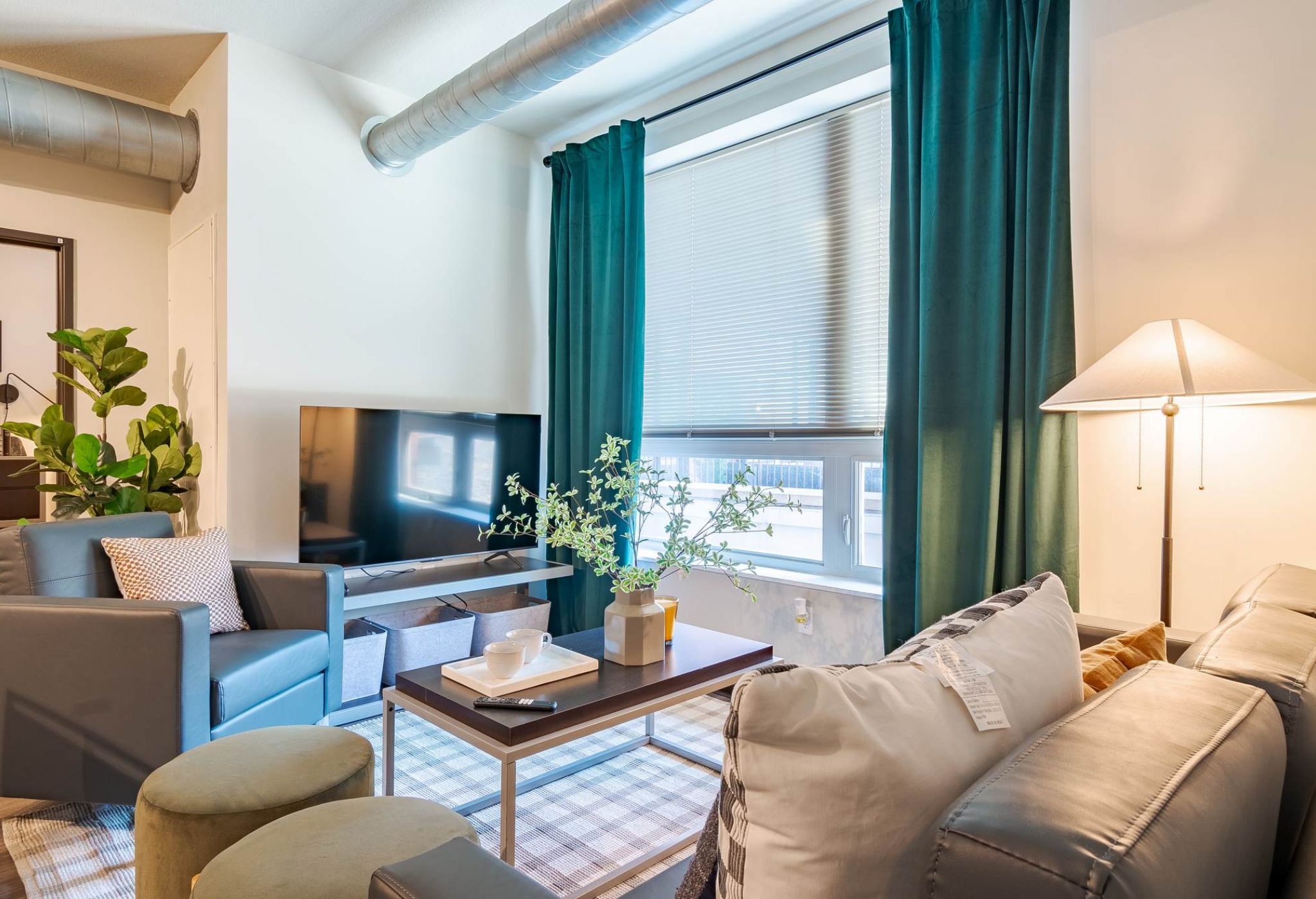 A bright modern living room featuring a cozy sofa, coffee table, and large windows with teal curtains, creating a welcoming space to relax at District Flats Columbia.