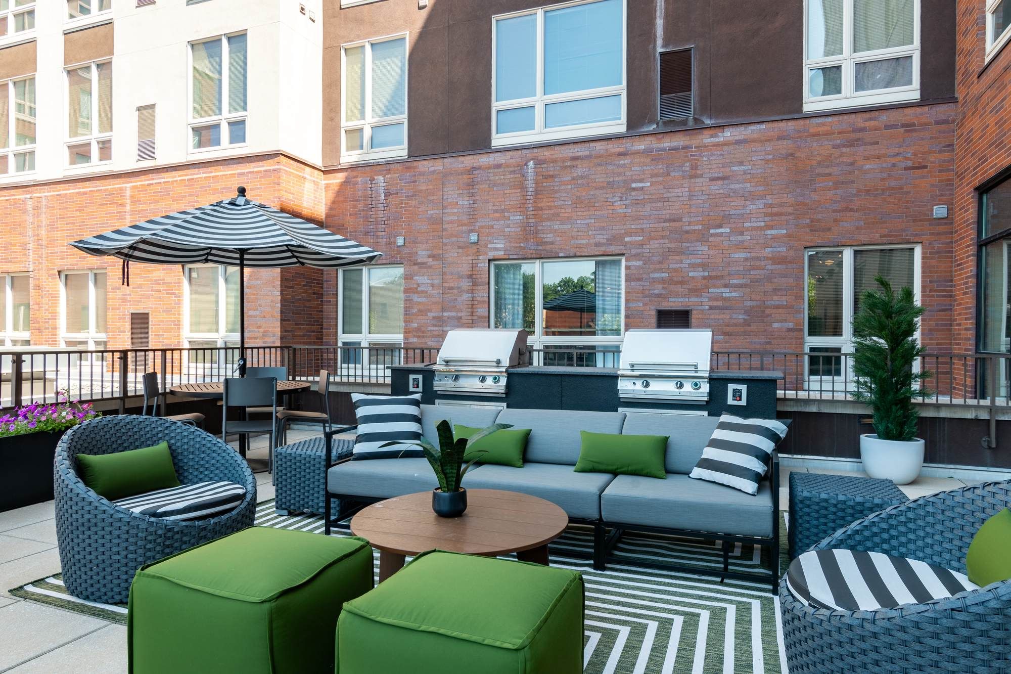 Outdoor lounge area at District Flats Columbia featuring modern patio furniture, green accent cushions, umbrellas, and built-in grills against a brick exterior backdrop.